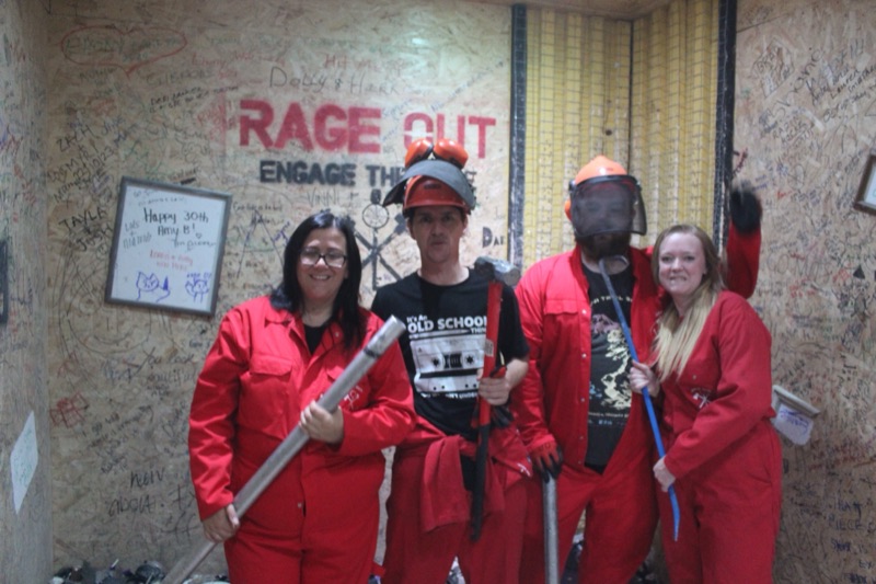 Group of four in red overalls with smashing tools under the Rage Out sign