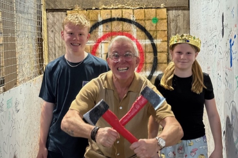 Family posing with foam axes in front of an axe throwing target